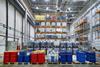 Oil drums and plastic container on pallets in a warehouse on metal shelving.